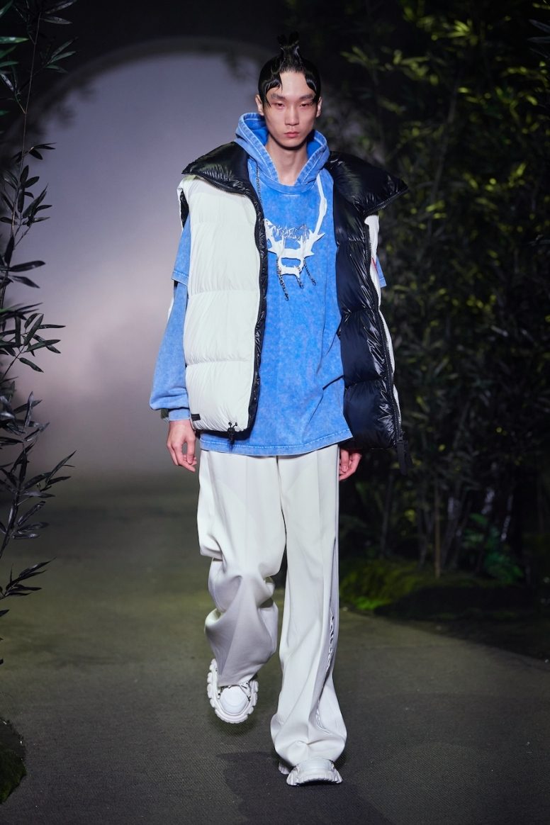 Модель идёт по подиуму среди тёмной листвы